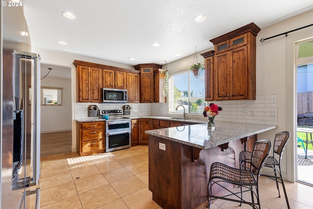 kitchen with decorative backsplash, sink, stainless steel appliances, light stone countertops, and light tile patterned floors