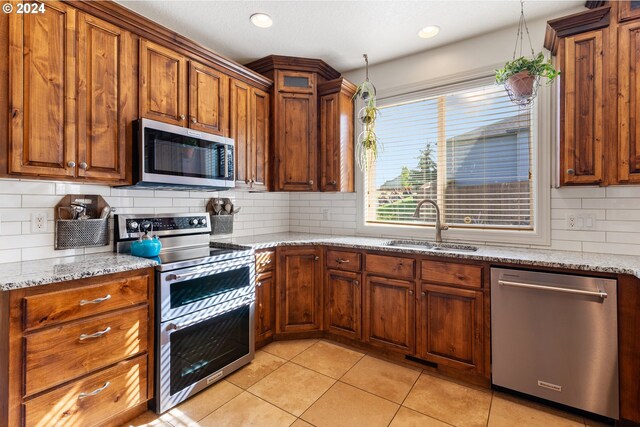 kitchen with light stone countertops, stainless steel appliances, sink, light tile patterned floors, and backsplash