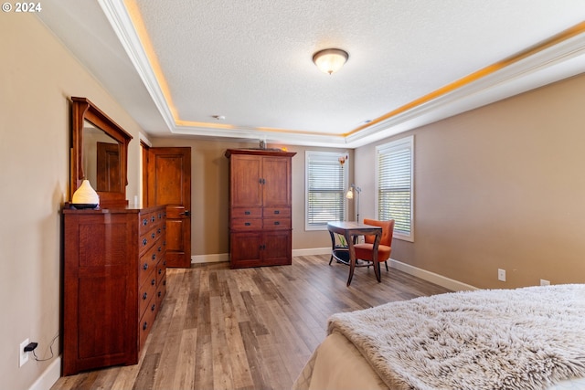 bedroom featuring ornamental molding, a textured ceiling, wood-type flooring, and a raised ceiling