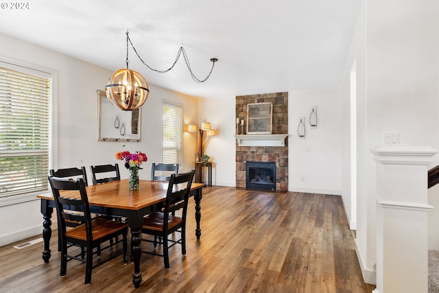 dining area with a stone fireplace, hardwood / wood-style flooring, and a chandelier