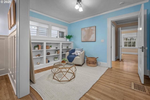 living area featuring visible vents, ornamental molding, light wood-style flooring, and baseboards