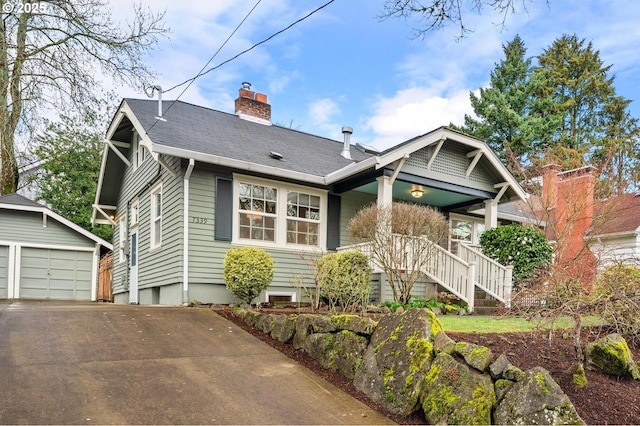 view of front of property featuring a shingled roof, a chimney, a detached garage, an outbuilding, and a porch