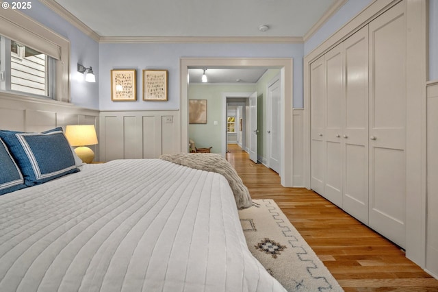 bedroom featuring ornamental molding, a wainscoted wall, a decorative wall, and light wood finished floors