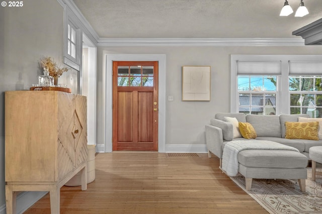 entrance foyer with ornamental molding, light wood finished floors, a textured ceiling, and baseboards