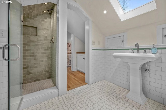 bathroom featuring lofted ceiling with skylight, a shower stall, tile walls, and a wainscoted wall