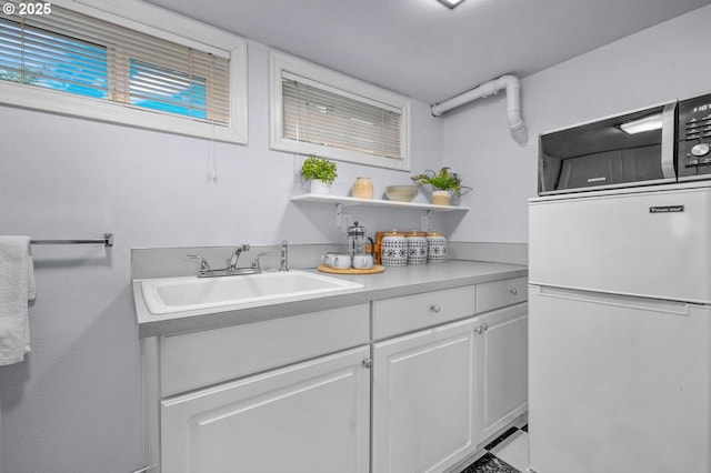 kitchen with open shelves, light countertops, freestanding refrigerator, white cabinets, and a sink