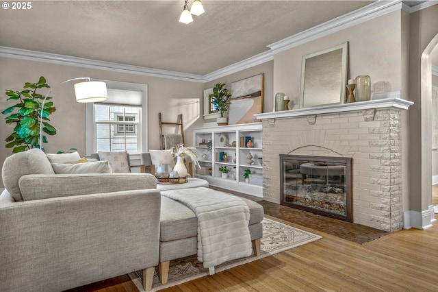 living area with ornamental molding, a brick fireplace, and wood finished floors