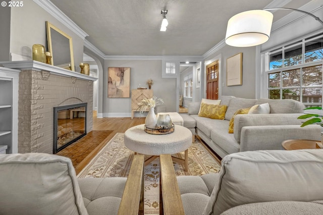 living area featuring baseboards, a fireplace, wood finished floors, and crown molding