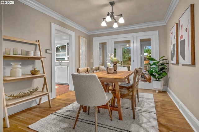 dining room featuring a notable chandelier, ornamental molding, light wood-type flooring, and baseboards