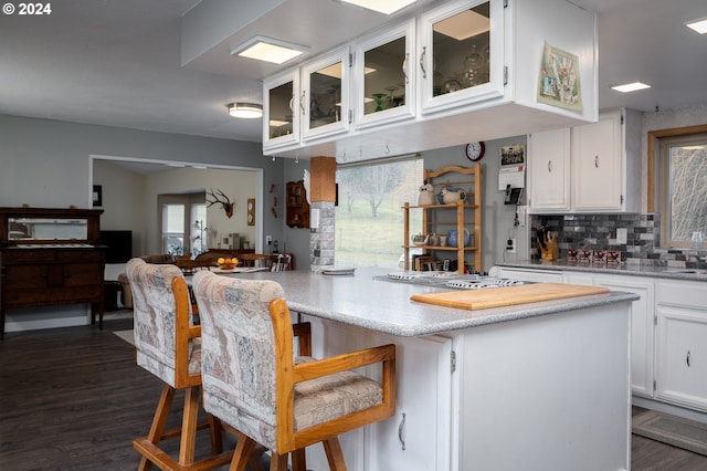 kitchen with backsplash, a breakfast bar, stainless steel gas cooktop, white cabinets, and dark hardwood / wood-style floors