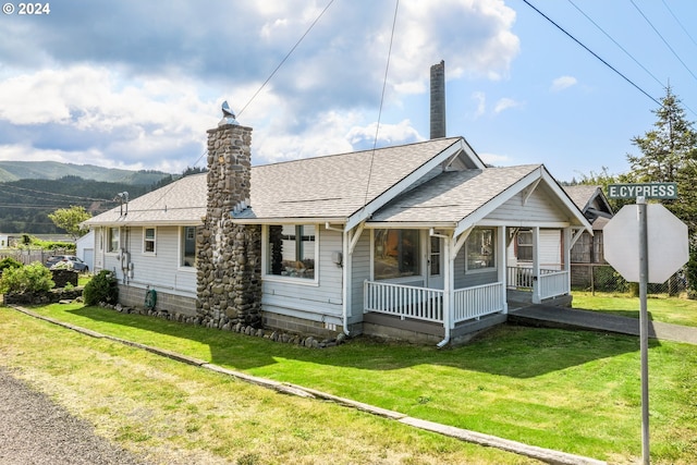 back of property with a mountain view, a yard, and covered porch