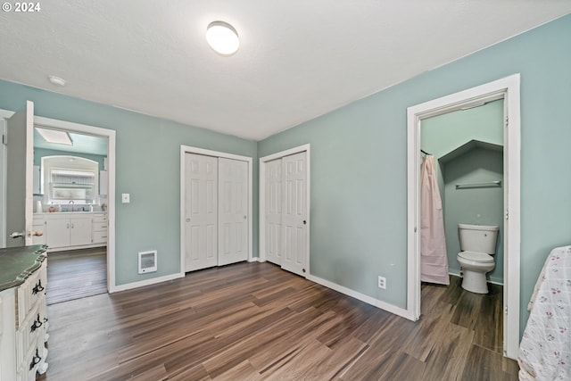 bedroom with dark hardwood / wood-style floors, ensuite bath, heating unit, and sink