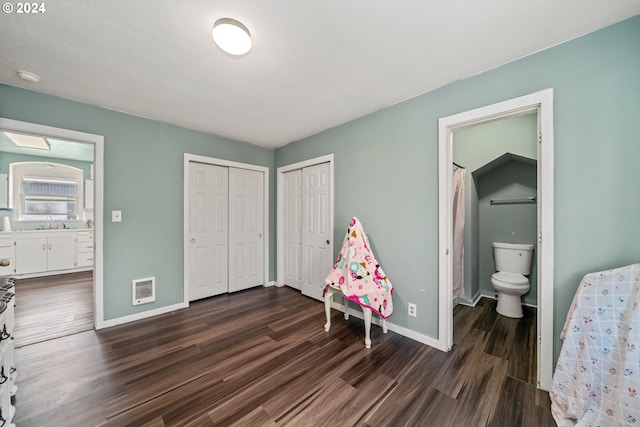 bedroom featuring two closets, dark wood-type flooring, and ensuite bathroom