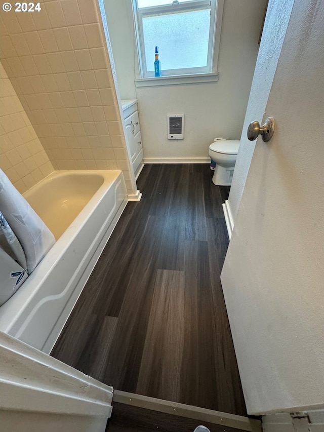 bathroom featuring heating unit, vanity, toilet, a bath, and hardwood / wood-style floors