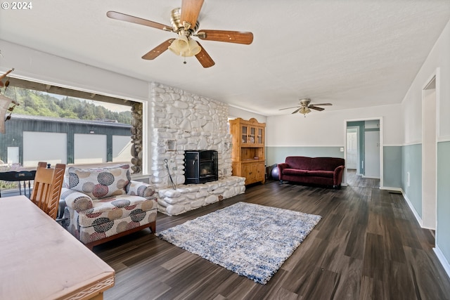 living room featuring dark hardwood / wood-style flooring, a textured ceiling, ceiling fan, and a stone fireplace