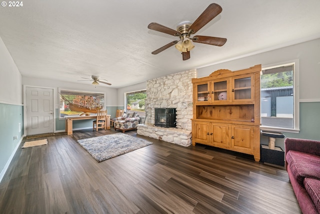 living room featuring ceiling fan, a stone fireplace, dark hardwood / wood-style flooring, and a healthy amount of sunlight