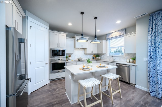 kitchen featuring stainless steel appliances, sink, decorative light fixtures, white cabinets, and a center island