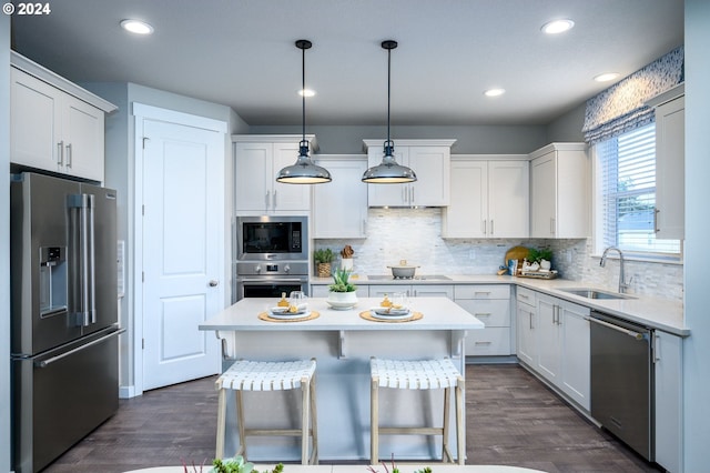 kitchen with appliances with stainless steel finishes, dark hardwood / wood-style flooring, a kitchen breakfast bar, pendant lighting, and white cabinetry