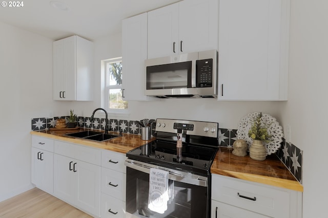 kitchen with appliances with stainless steel finishes, light hardwood / wood-style flooring, white cabinets, and sink