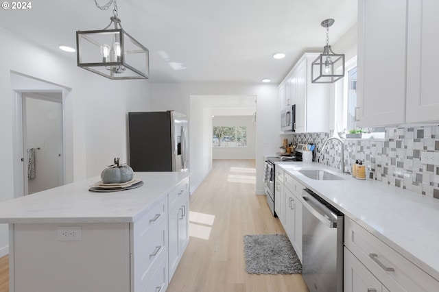 kitchen featuring appliances with stainless steel finishes, light hardwood / wood-style flooring, hanging light fixtures, white cabinetry, and a center island