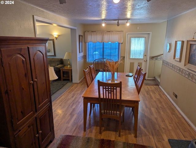 dining space featuring light hardwood / wood-style floors, a textured ceiling, and track lighting