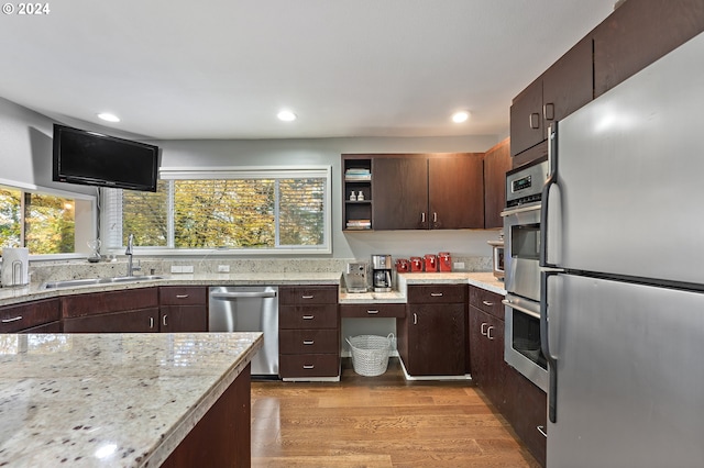 kitchen with sink, appliances with stainless steel finishes, dark brown cabinets, light wood-type flooring, and light stone countertops