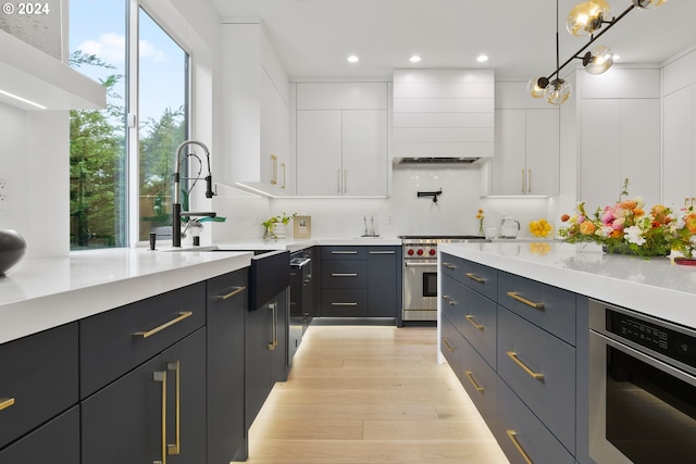 kitchen with pendant lighting, white cabinetry, appliances with stainless steel finishes, range hood, and light wood-type flooring