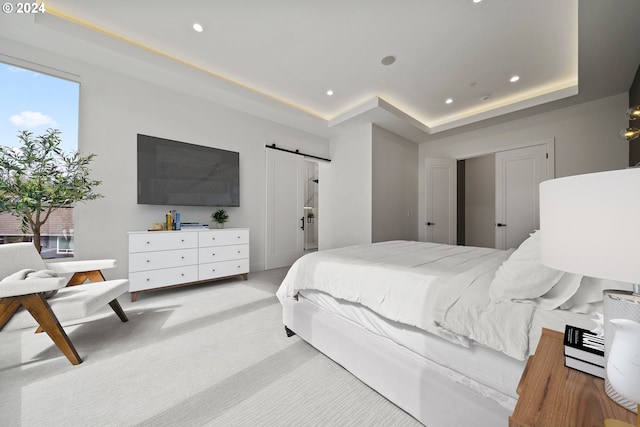 bedroom featuring light colored carpet, a tray ceiling, and a barn door