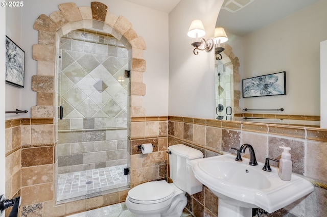 bathroom featuring sink, a shower with door, tile walls, and toilet