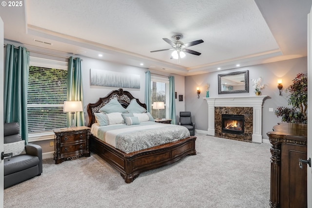 carpeted bedroom with ceiling fan, a raised ceiling, and a premium fireplace