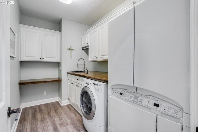 laundry area featuring cabinets, separate washer and dryer, sink, and light hardwood / wood-style flooring