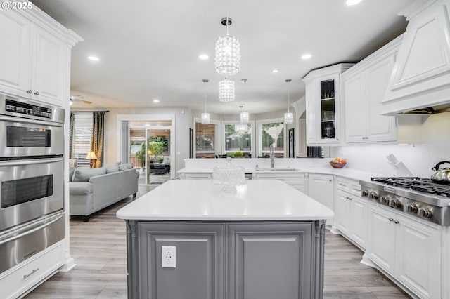 kitchen featuring pendant lighting, custom range hood, white cabinetry, kitchen peninsula, and stainless steel appliances