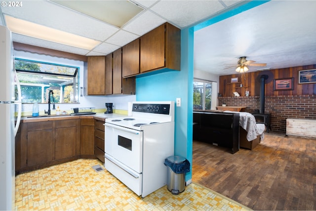 kitchen featuring light hardwood / wood-style flooring, a wood stove, a paneled ceiling, white appliances, and ceiling fan