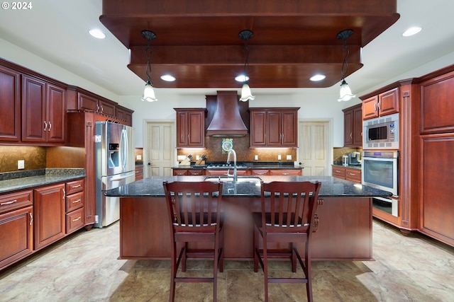 kitchen with custom range hood, backsplash, stainless steel appliances, and an island with sink