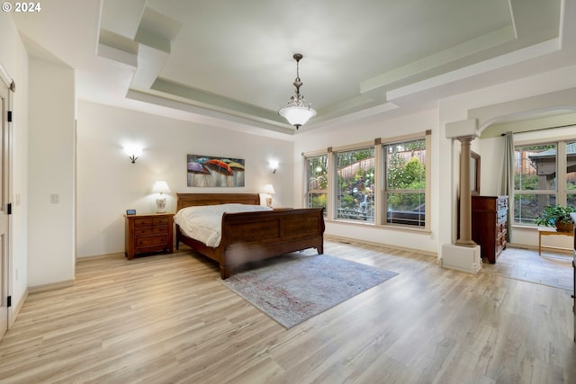 bedroom with light hardwood / wood-style floors, a raised ceiling, and ornate columns