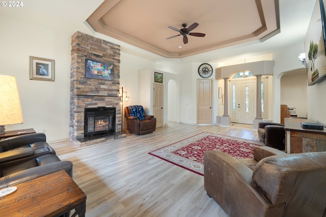 living room with ceiling fan, a raised ceiling, light wood-type flooring, and decorative columns