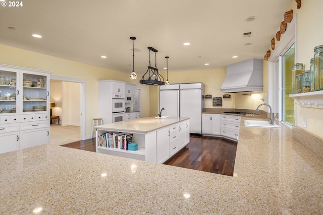 kitchen with sink, light stone counters, dark hardwood / wood-style flooring, pendant lighting, and custom exhaust hood