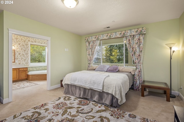 bedroom featuring ensuite bathroom, light colored carpet, a textured ceiling, and multiple windows