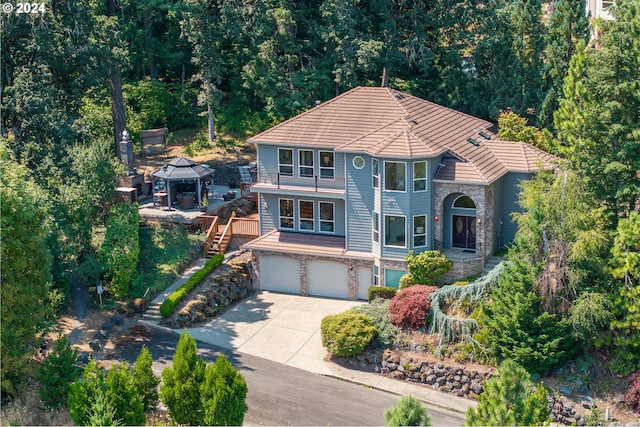 view of front facade with driveway, an attached garage, a gazebo, stone siding, and a tile roof