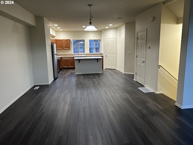 kitchen with stainless steel fridge, a textured ceiling, dark wood-type flooring, a kitchen island, and hanging light fixtures