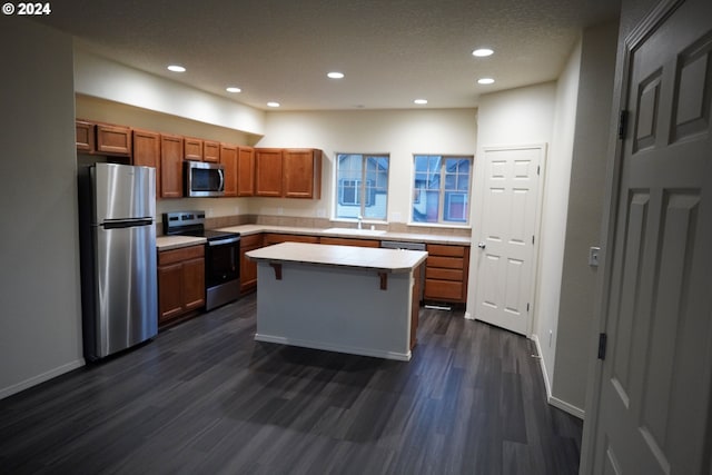 kitchen featuring sink, stainless steel appliances, dark hardwood / wood-style flooring, a textured ceiling, and a kitchen island