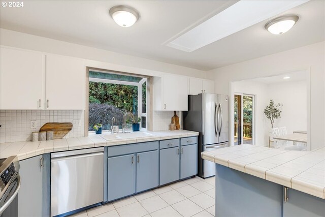 kitchen with white cabinets, tile counters, appliances with stainless steel finishes, and decorative backsplash