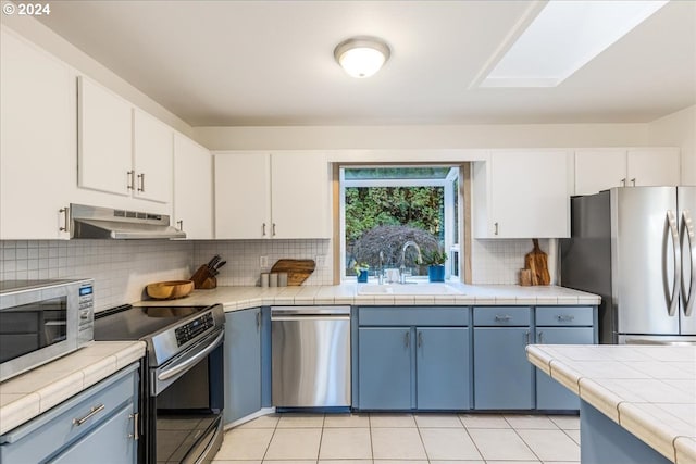 kitchen featuring appliances with stainless steel finishes, tile counters, white cabinetry, sink, and blue cabinetry