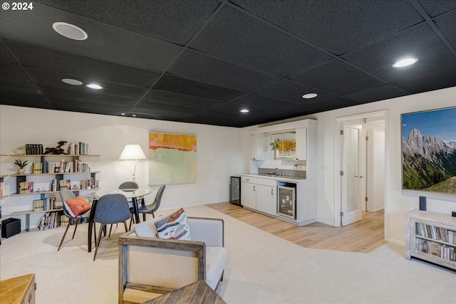 living room featuring indoor wet bar, a drop ceiling, beverage cooler, and light carpet