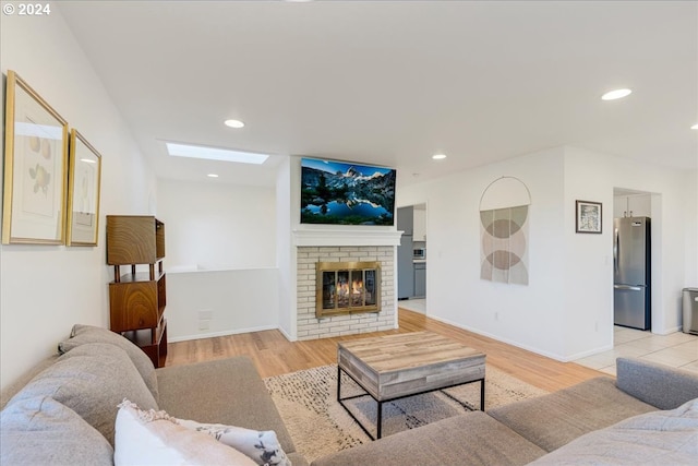 living room with a brick fireplace, light hardwood / wood-style floors, and a skylight