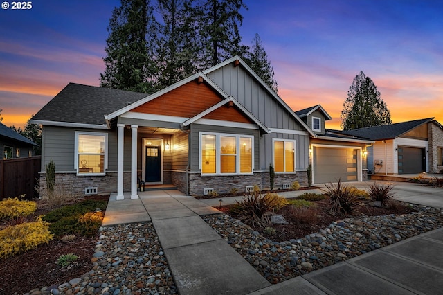 craftsman house with fence, driveway, stone siding, a garage, and board and batten siding