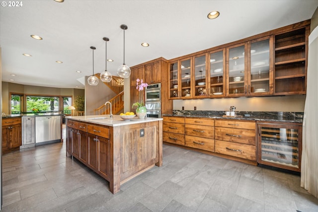 kitchen featuring a kitchen island with sink, hanging light fixtures, sink, wine cooler, and stainless steel appliances