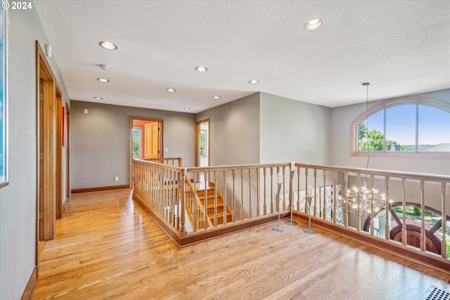 corridor featuring light hardwood / wood-style flooring, a textured ceiling, and a notable chandelier