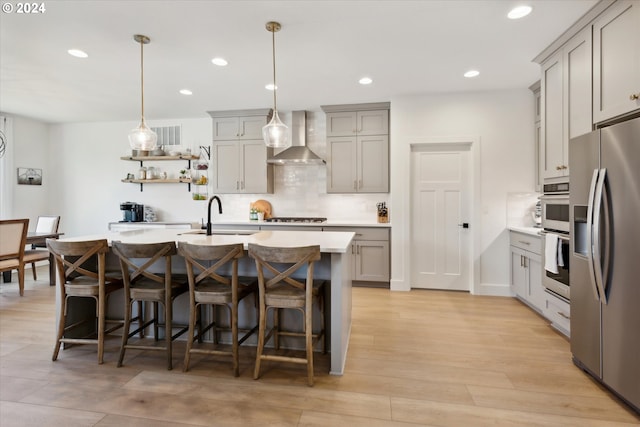 kitchen featuring wall chimney exhaust hood, stainless steel appliances, sink, decorative light fixtures, and light hardwood / wood-style floors