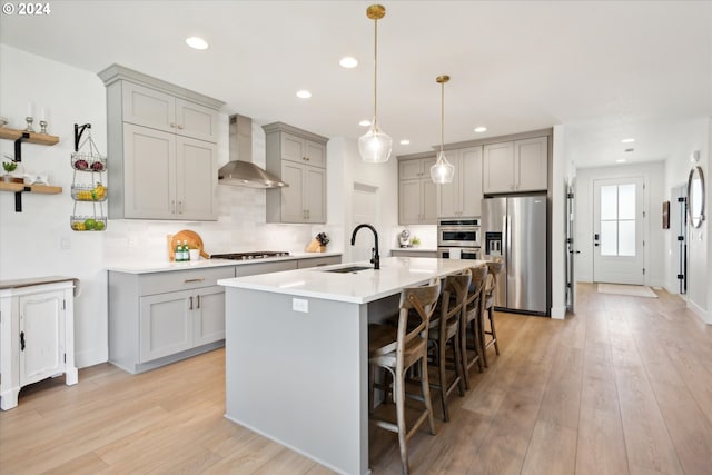 kitchen featuring appliances with stainless steel finishes, a kitchen breakfast bar, light hardwood / wood-style flooring, wall chimney exhaust hood, and sink